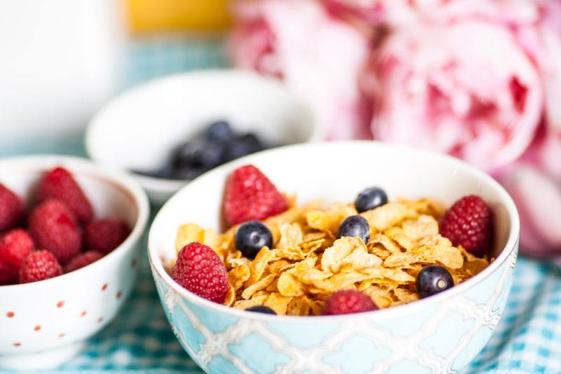 A bowl of cereal next to bowls of fresh fruit