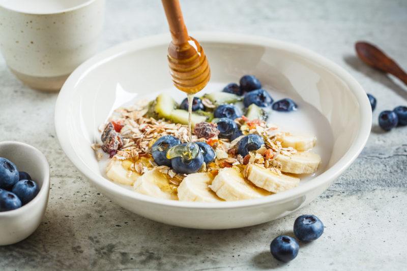 A white bowl with cereal, fruit, and honey