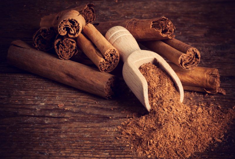 Ceylon cinnamon quills on a table with cinnamon powder spilling out of a scoop