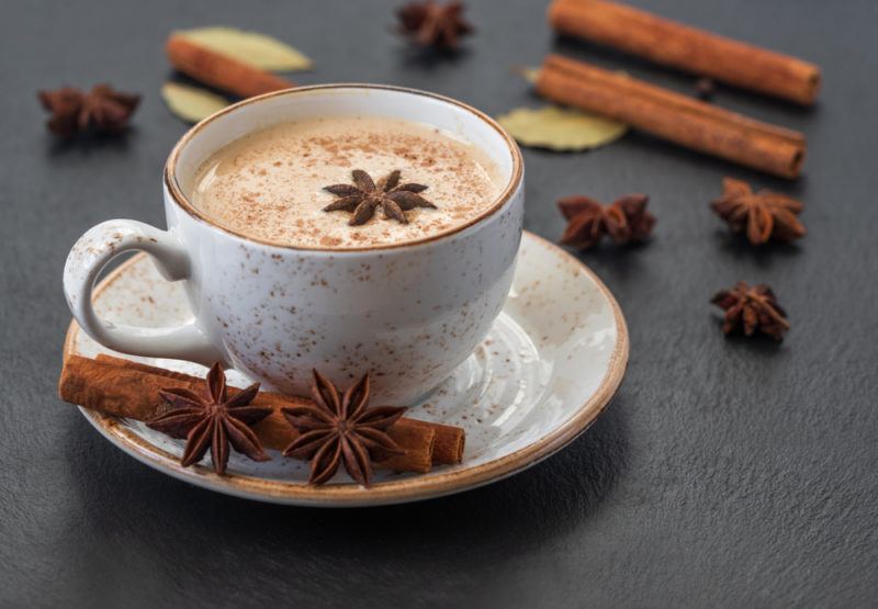 A mug of chai tea with cinnamon sticks and star anise on the saucer and the table