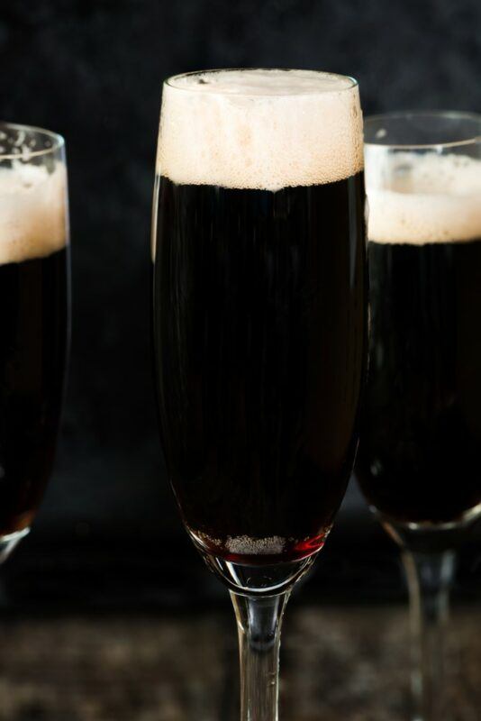 Three champagne glasses containing a black velvet cocktail against a dark background