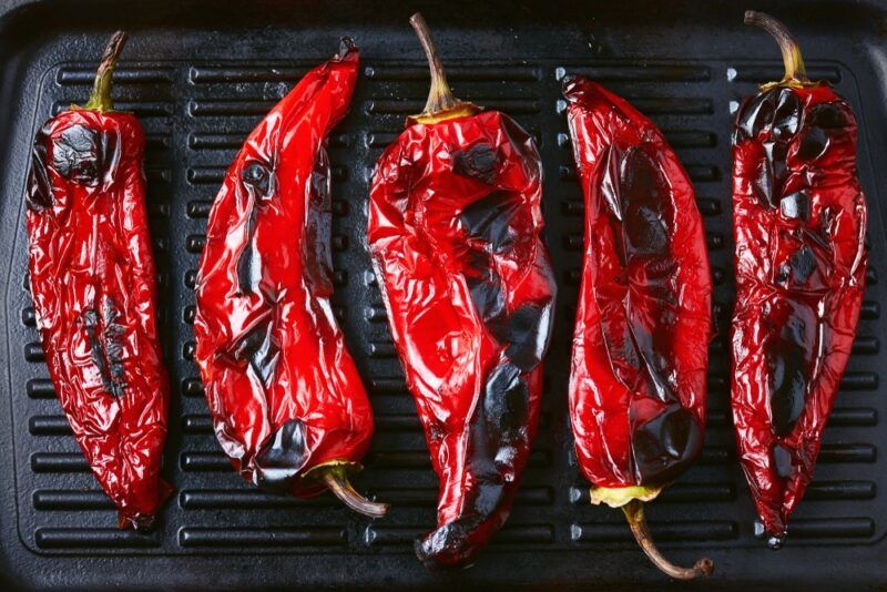 A grill with five chargrilled red peppers on top