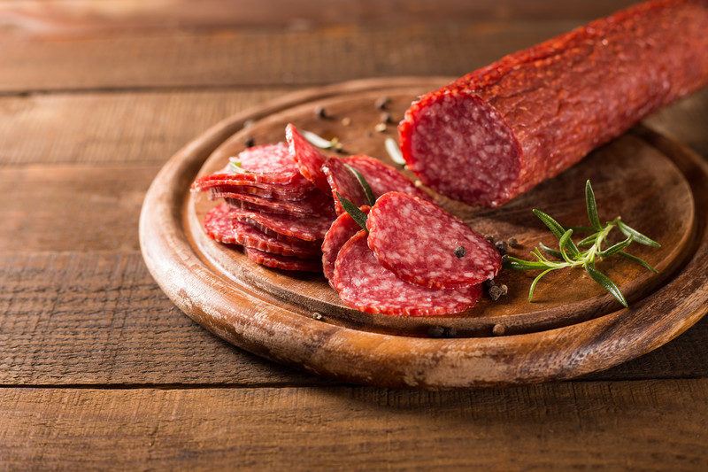 A round wooden plate with a stick of salami and some sliced salami