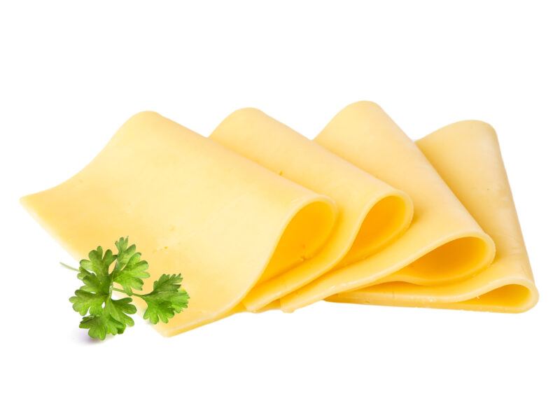 This photo shows four slices of cheese and a sprig of parsley against a white background.