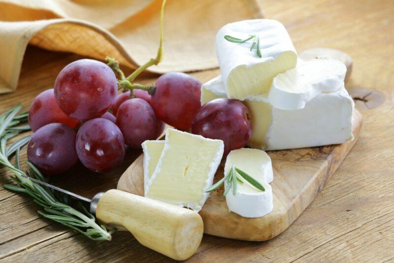 A wooden table with a board, some fresh cheese, and grapes