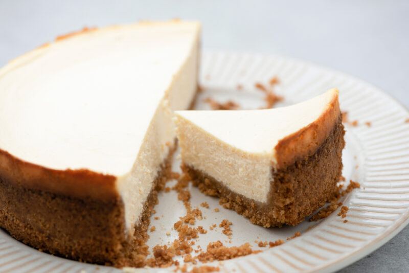 on a white ceramic plate is a partially sliced New York cheesecake