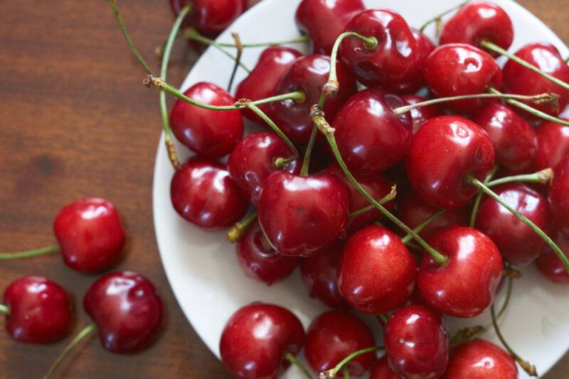 Fresh,Red,Cherries,Fruit,On,Plate,On,Wooden,Background,Close | Food For Net This photo shows an overhead view of a white bowl filled with fresh cherries, resting on a wooden surface near three more cherries.