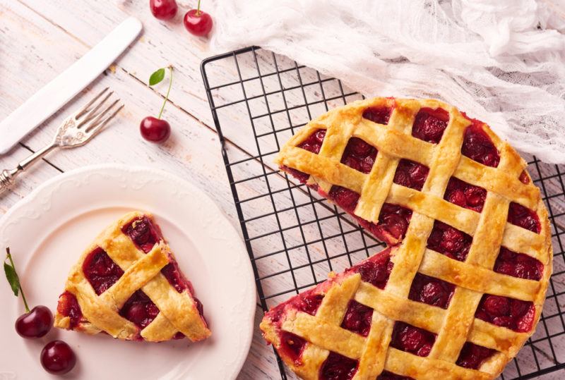 A cherry pie cooling on a rack with one piece cut out of it on a white plate