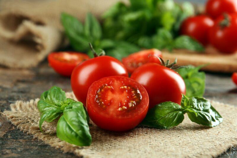 A mat on a wooden table with some cut tomatoes and basil