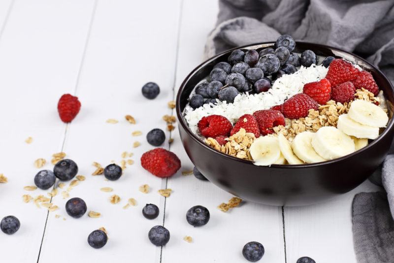 A black breakfast bowl that includes sliced fruit and berries