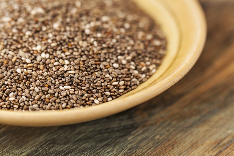 This photo shows a closeup of a yellow bowl of chia seeds on a wooden table.