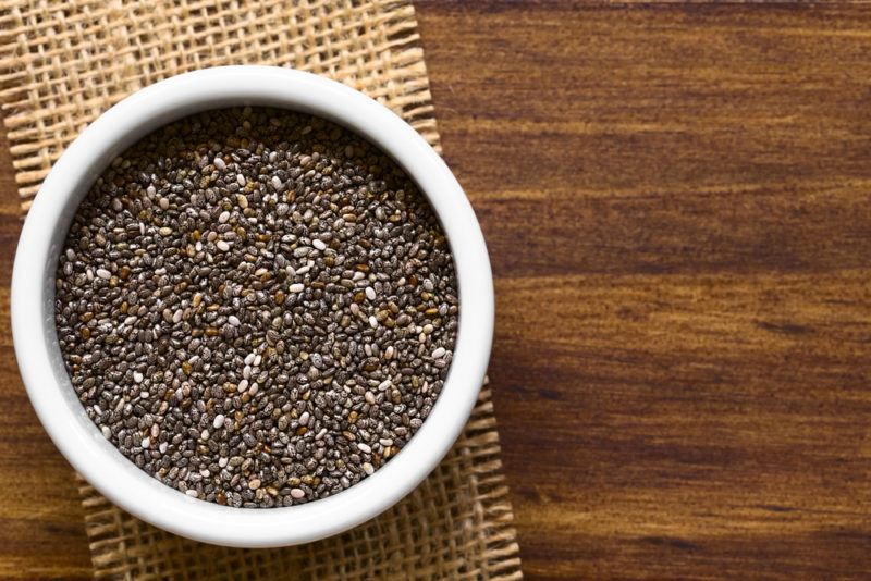 A white bowl on a wooden table containing chia seeds