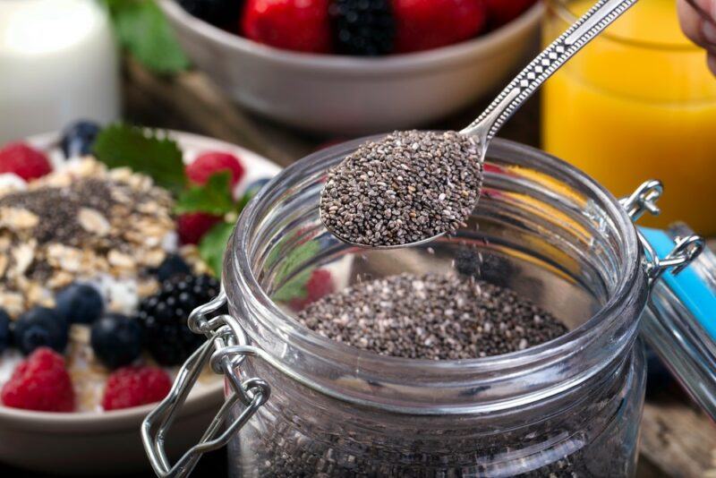 A glass jar filled with chia seeds with a spoon scooping some out