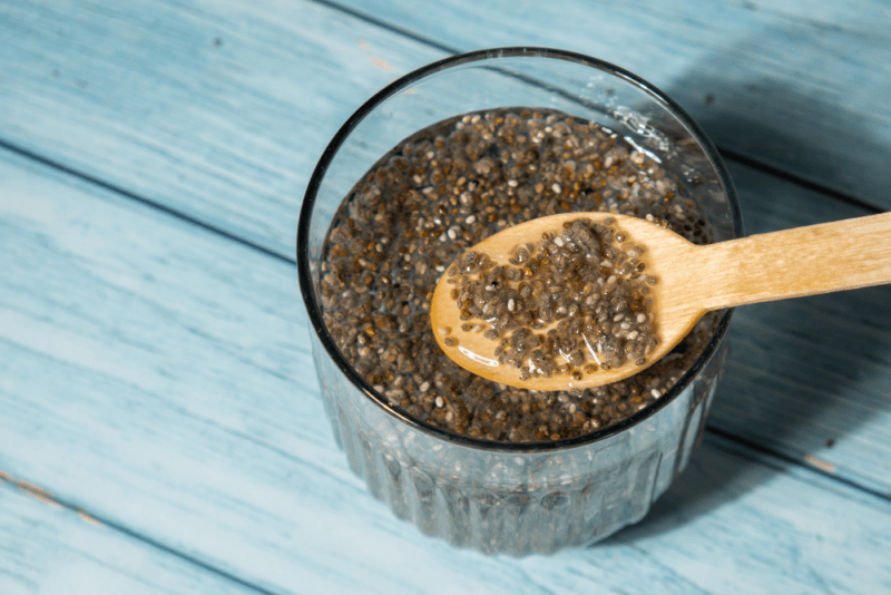 A glass containing chia seeds and water, where a wooden spoon is being used to lift some of the chia seeds out