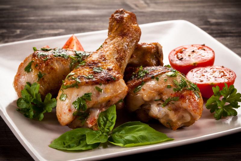 A white square plate with chicken drumsticks, greens and tomatoes