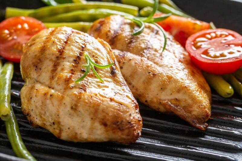 A grill with two pieces of cooked chicken breast, plus tomatoes and asparagus