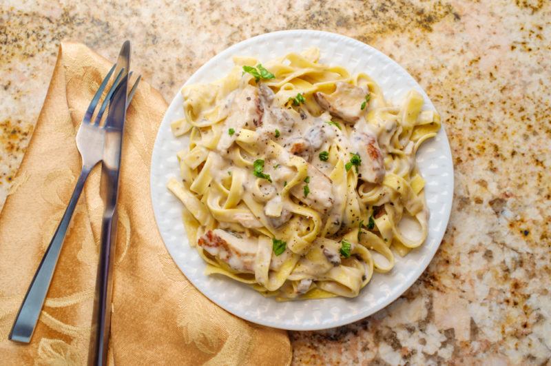 A white place with chicken fettuccine and a knife and fork