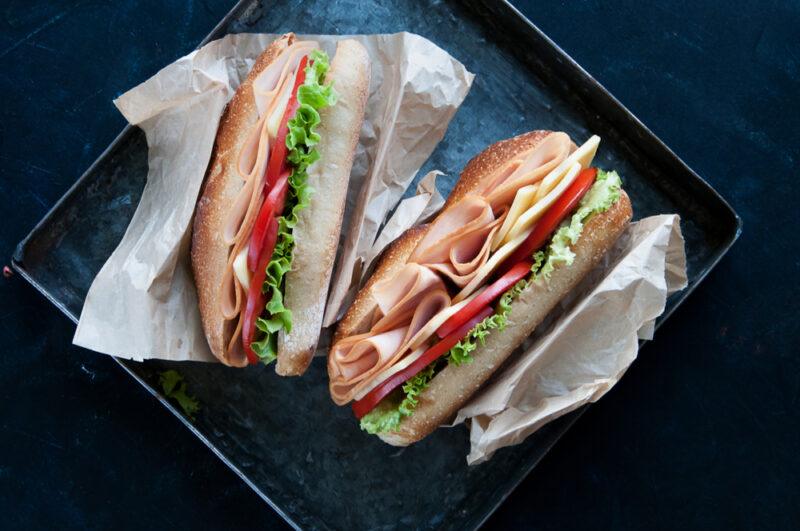 Two sandwiches wrapped in paper filled with sliced chicken and plenty of vegetables