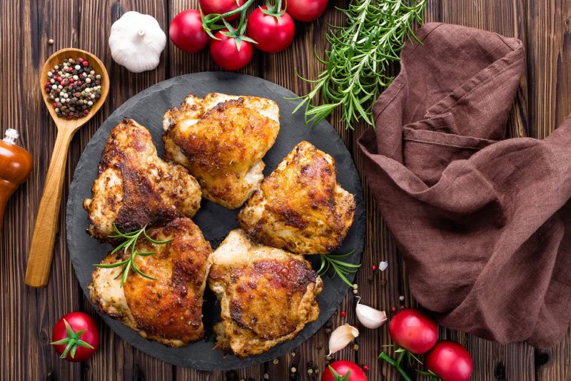 Cooked chicken thighs on a black plate with tomatoes surrounding it