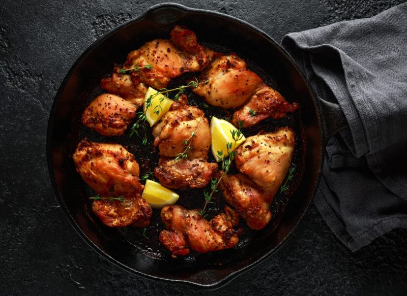 A cast iron black frypan containing chicken thighs