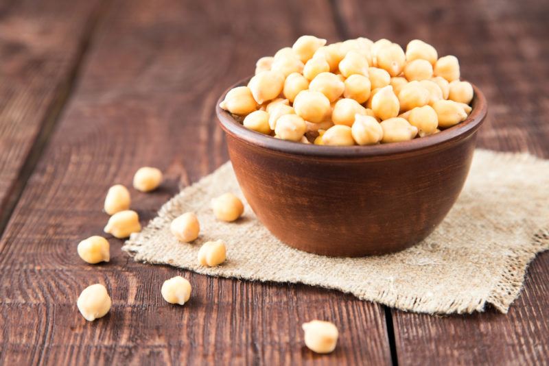 A wooden bowl of chickpeas with a few chickpeas on the table