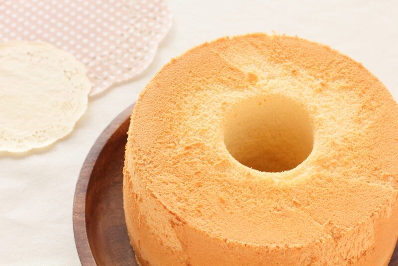 a closeup image of a wooden plate with a round chiffon cake with a whole in the middle