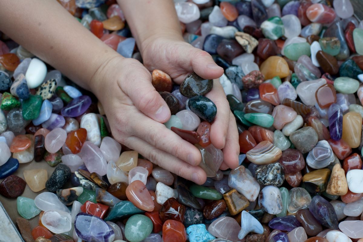 hilds hands holding polished rocks above a multitude of various polished rocks in a box