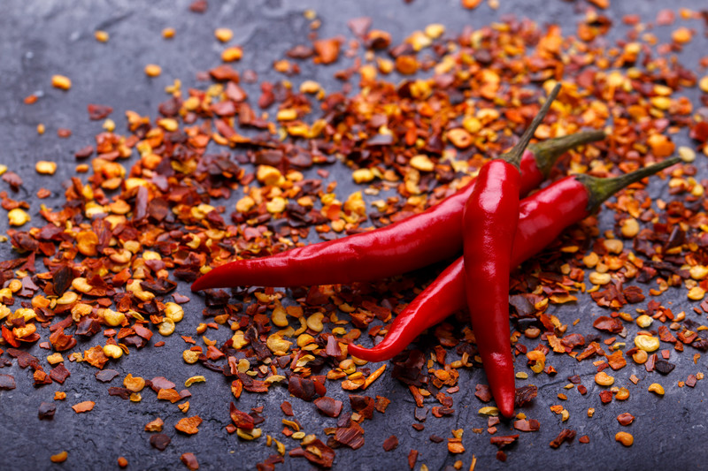 top view image of chili flakes with 3 fresh chilis on top of a dark surface