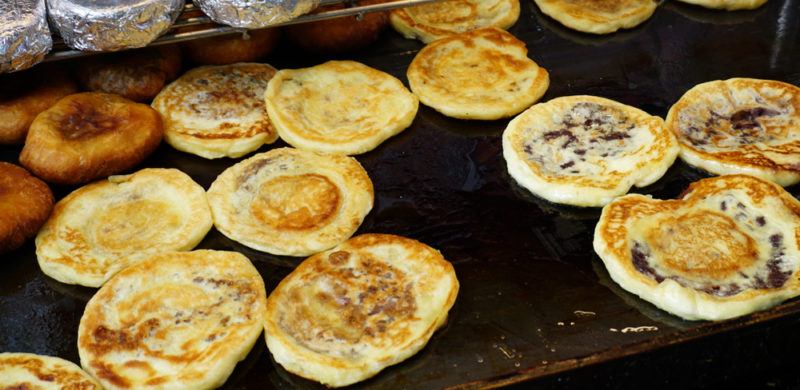 Various Chinese pancakes with different fillings being cooked on a grill