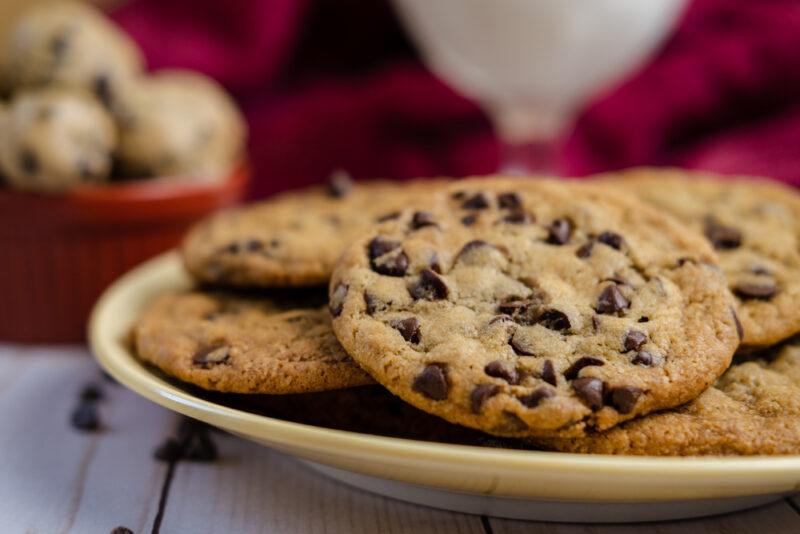 A plate of chocolate chip cookies rests on a wooden surface.