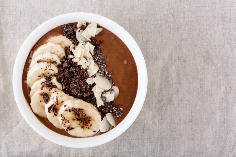 A white bowl that contains a chocolate smoothie with sliced bananas on top