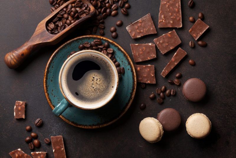 A black coffee next to coffee beans, cocolate and biscuits