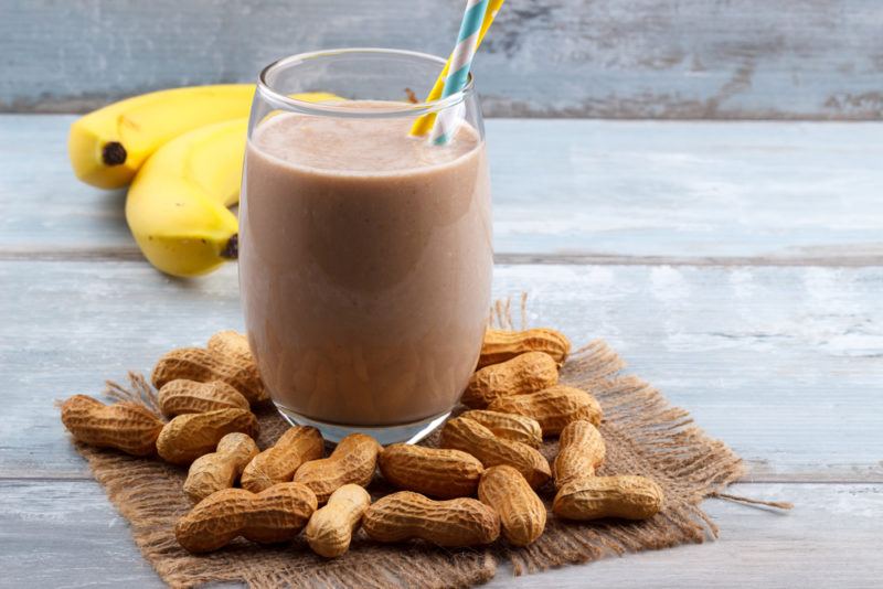 Chocolate, banana and nut butter smoothie in a glass with nuts and bananas