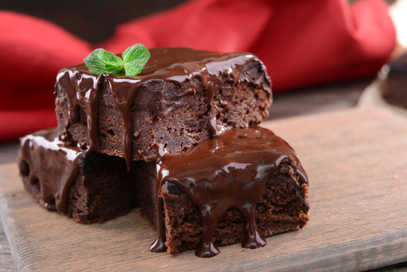 A stack of three chocolate brownies covered in chocolate sauce