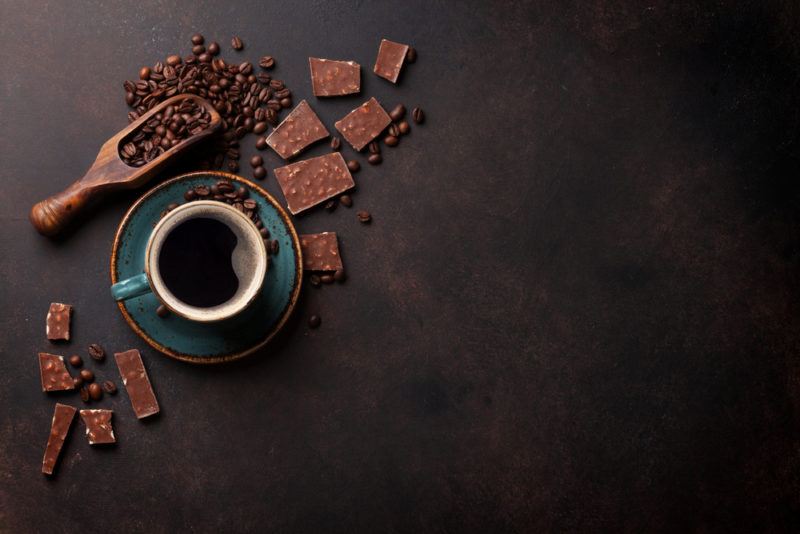 A mug of coffee, a scoop of coffee beans, and various pieces of chocolate with coffee