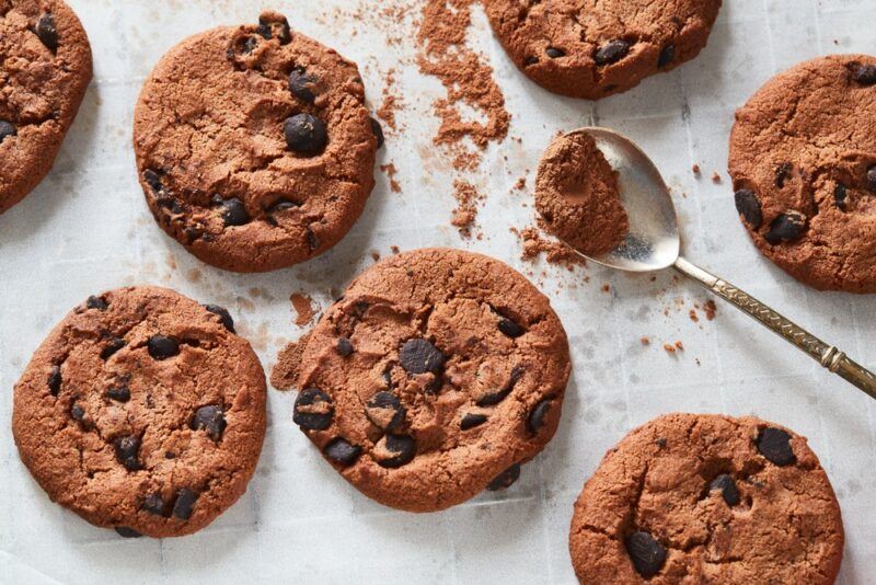 A selection of chocolate chip cookies on a table with a spoon of cocoa powder