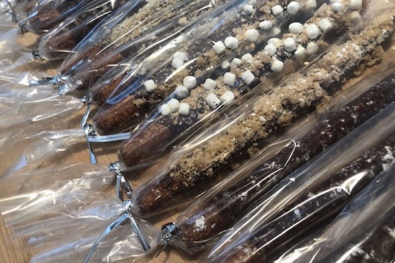 An assortment of individually wrapped chocolate covered pretzel rods with various toppings