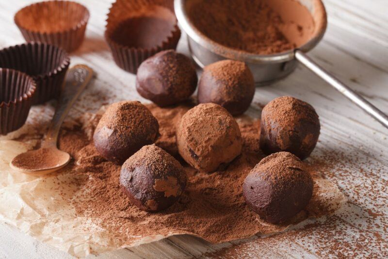 A selection of chocolate cream cheese truffles that have been rolled in cocoa powder. There are also some cupdake liners and a container of cocoa powder.