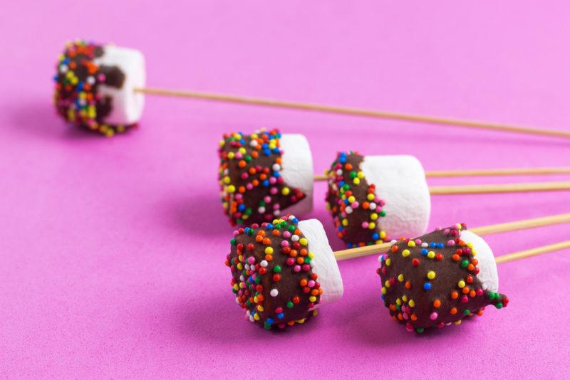 A selection of marshmallows on sticks that have been dipped in chocolate and sprinkles