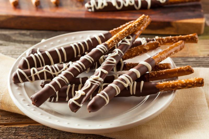 A white plate of pretzels that have been dipped in chocolate, with lines of white chocolate