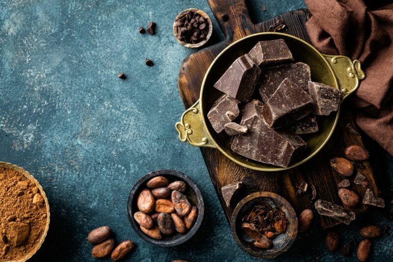 A blue table with a selection of bowls of dark chocolate and some cocoa powder