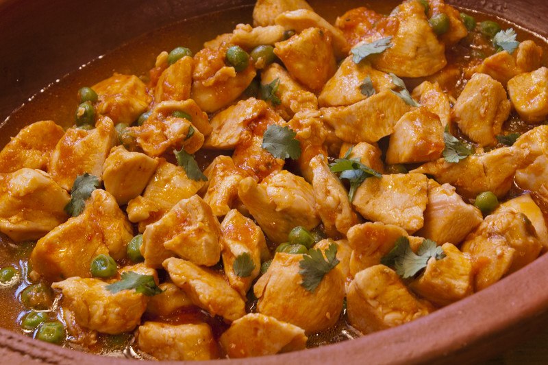 A brown dish is filled with cooked chopped chicken and parsley leaves.