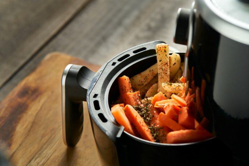 A black air fryer with chopped carrots and parsnips