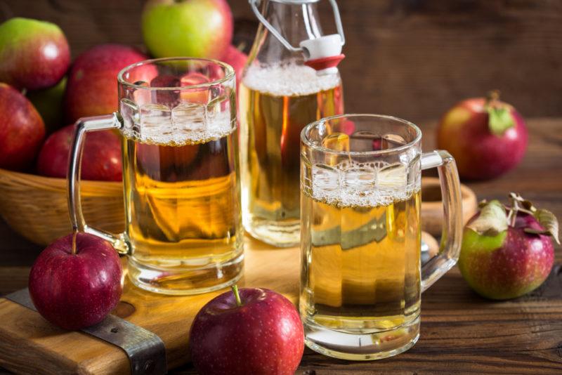 Two pint glasses and a bottle of hard cider with apples in the background