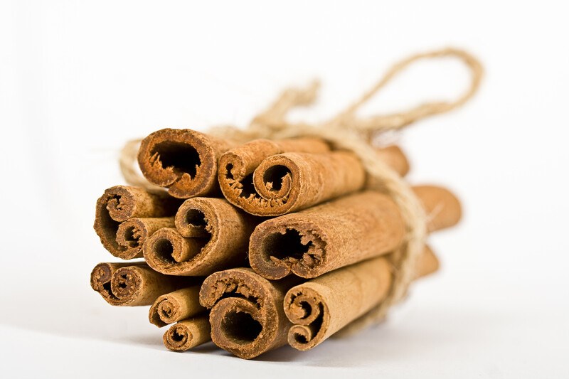 Several cinnamon sticks tied with twine rest on a white surface against a white background.