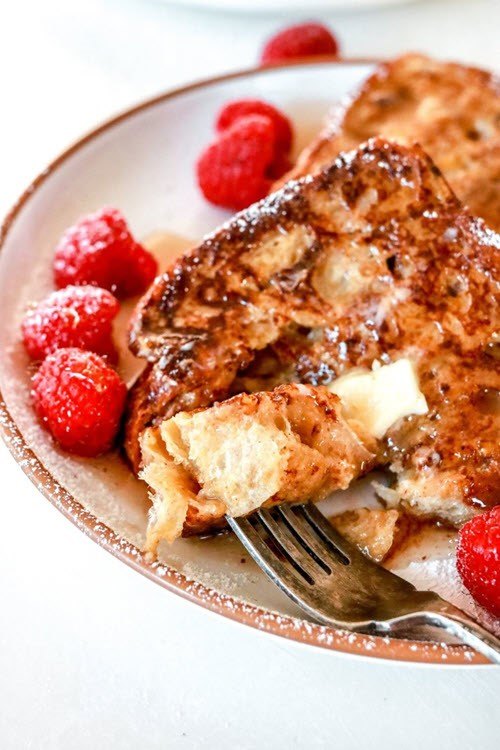 A white dish containing cinnamon French toast with raspberries