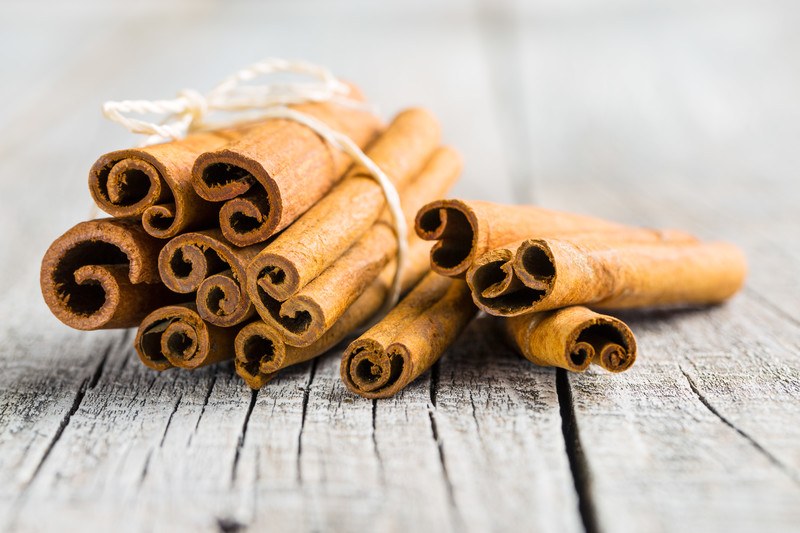 Closeup image of a bundle of cinnamon sticks tied with a string with a few sticks beside it, resting on a wooden table.