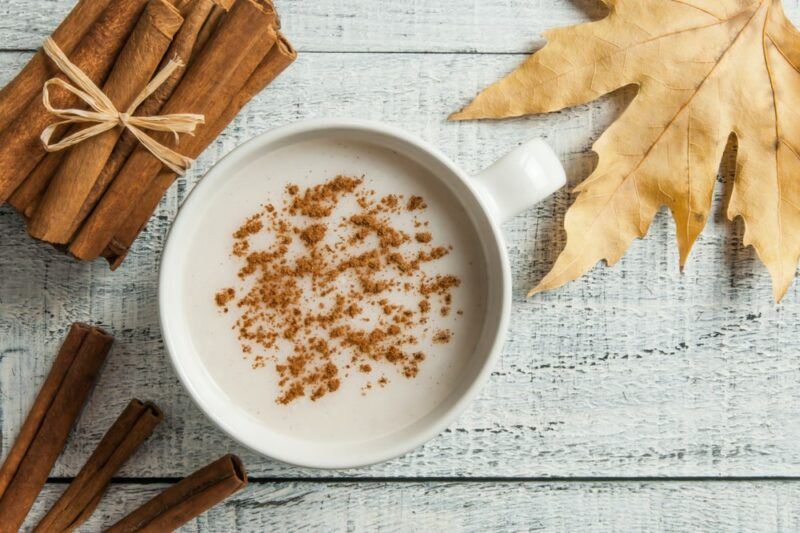 A white table with cinnamon sticks, a leafy, and porridge topped with cinnamon