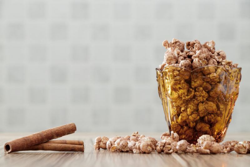 A glass container of popcorn next to cinnamon sticks