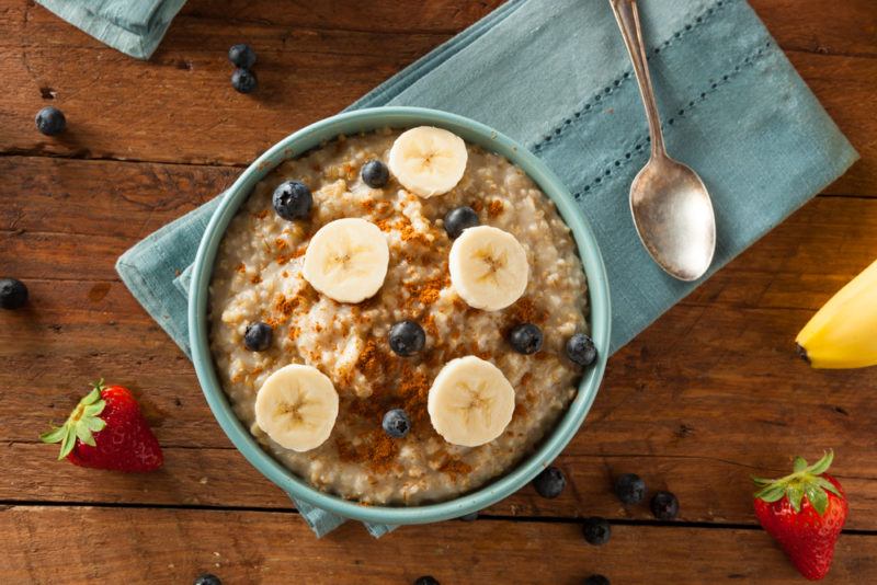 A blue bowl containing cooked porridge, bananas and blueberries